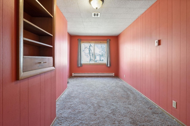 spare room featuring visible vents, a baseboard heating unit, wood walls, and carpet