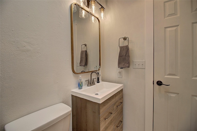 bathroom featuring toilet, a textured wall, and vanity