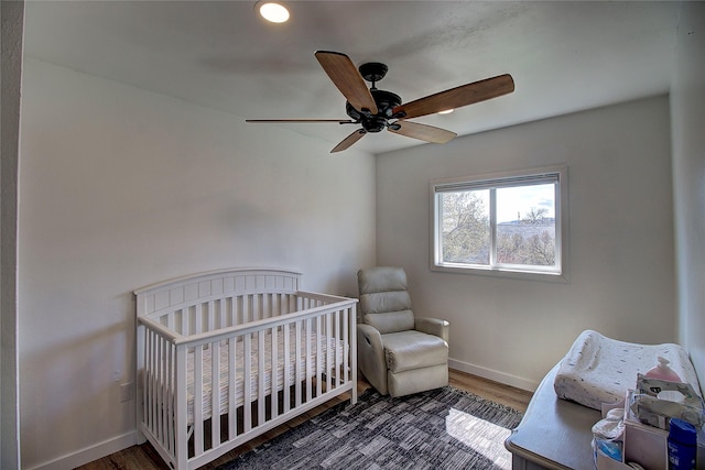 bedroom with recessed lighting, ceiling fan, a nursery area, baseboards, and wood finished floors