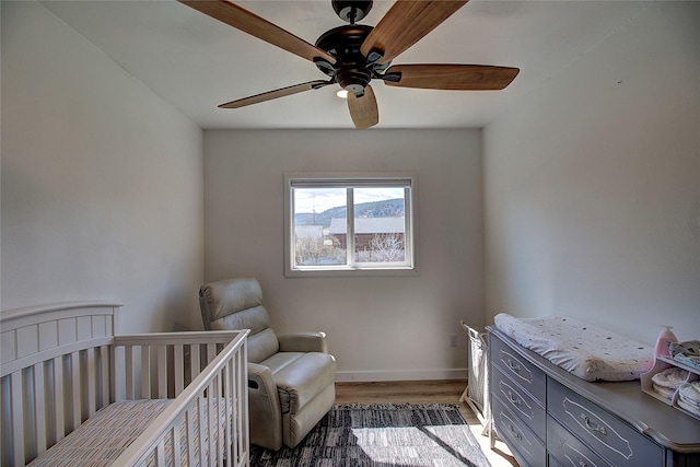 bedroom with wood finished floors, ceiling fan, baseboards, and a crib