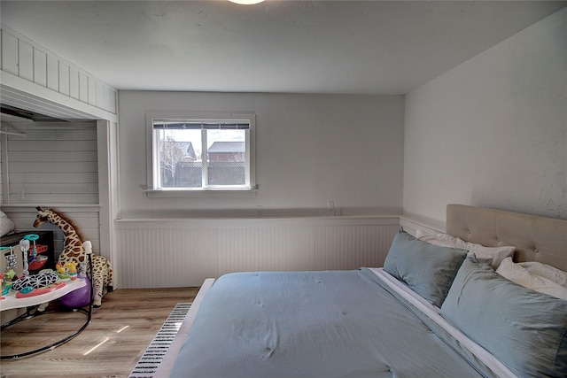 bedroom featuring light wood finished floors and a wainscoted wall