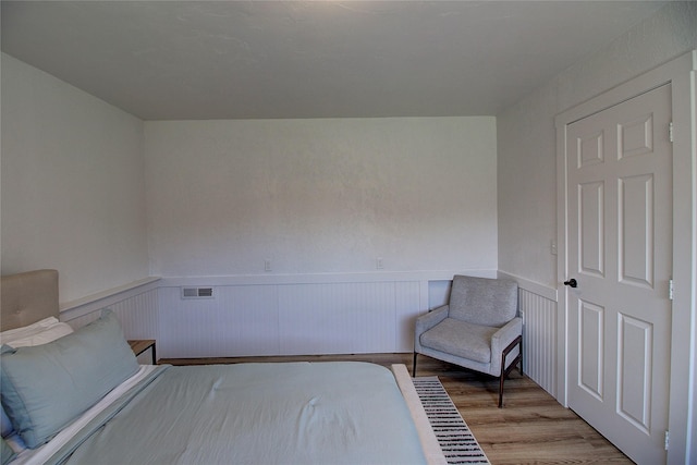 bedroom featuring a wainscoted wall, visible vents, and light wood-style floors