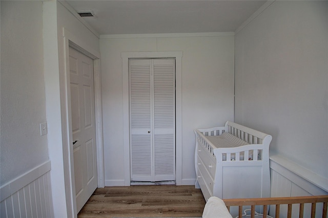bedroom featuring wood finished floors, a closet, visible vents, and wainscoting