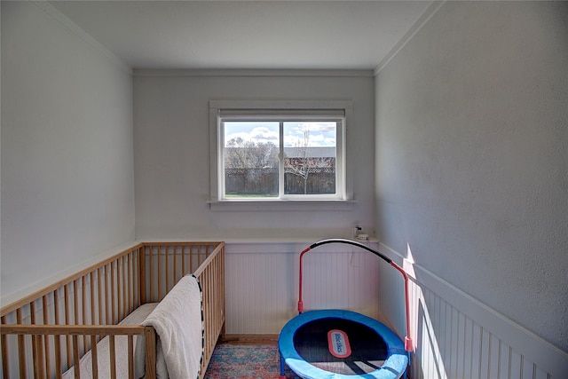 bedroom with ornamental molding, a nursery area, and wainscoting