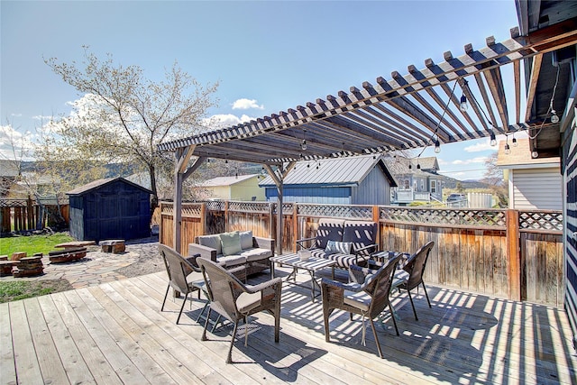 wooden terrace featuring a pergola, an outdoor structure, a fenced backyard, an outdoor living space with a fire pit, and a storage unit