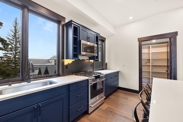 kitchen with blue cabinetry, stainless steel appliances, light wood-style floors, light countertops, and a sink