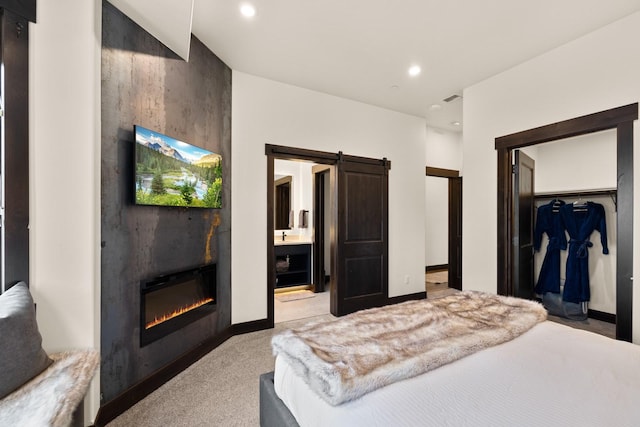 bedroom featuring recessed lighting, a barn door, a closet, a glass covered fireplace, and light carpet
