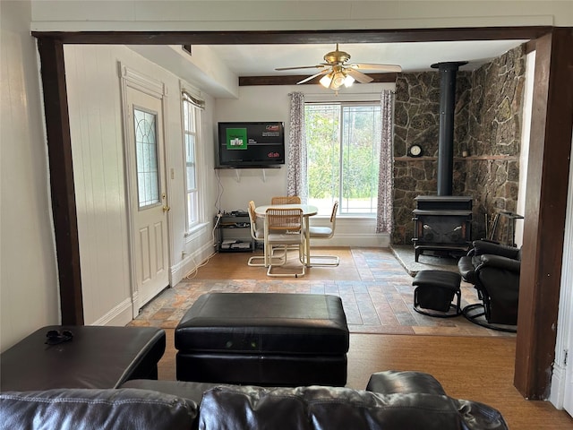 living area with wood finished floors, ceiling fan, a wood stove, and baseboards