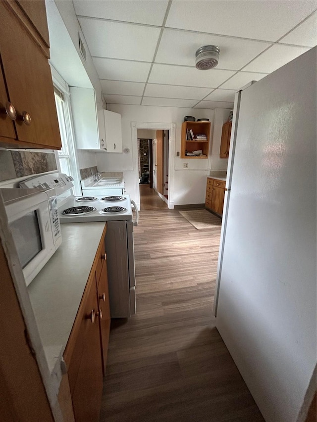 kitchen featuring brown cabinetry, a drop ceiling, wood finished floors, and white appliances