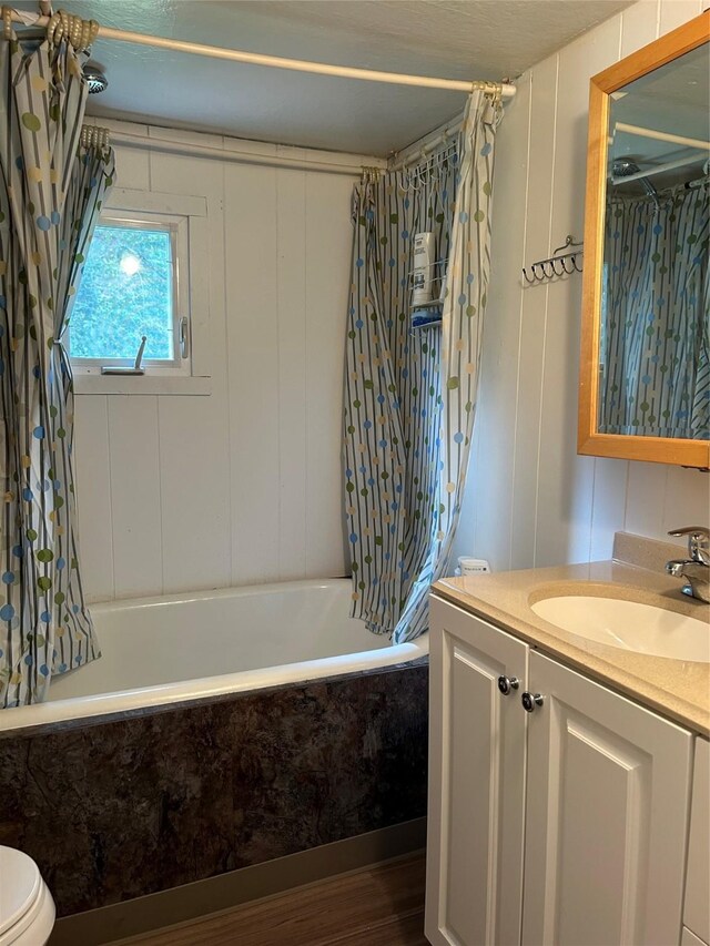 bathroom with a decorative wall, shower / bath combo with shower curtain, toilet, wood finished floors, and vanity