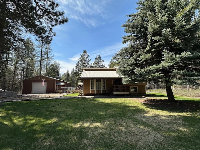 back of house with a porch, a yard, an outbuilding, metal roof, and a detached garage