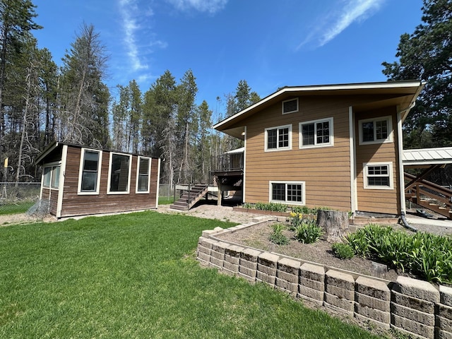 back of house featuring a deck, fence, an outbuilding, stairs, and a lawn