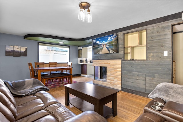 living area with wood walls, baseboards, light wood finished floors, and a brick fireplace