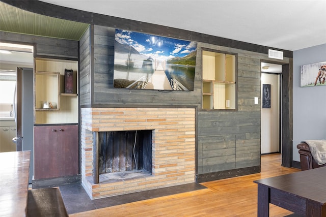 living room featuring visible vents, wood finished floors, and a brick fireplace