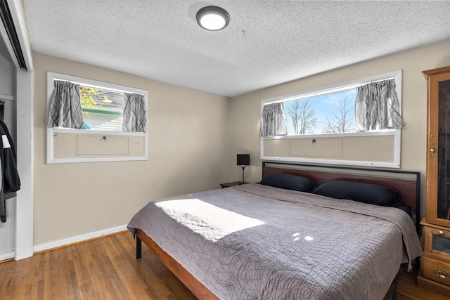 bedroom with a textured ceiling, wood finished floors, and baseboards