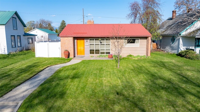 bungalow with a chimney, metal roof, fence, brick siding, and a front lawn