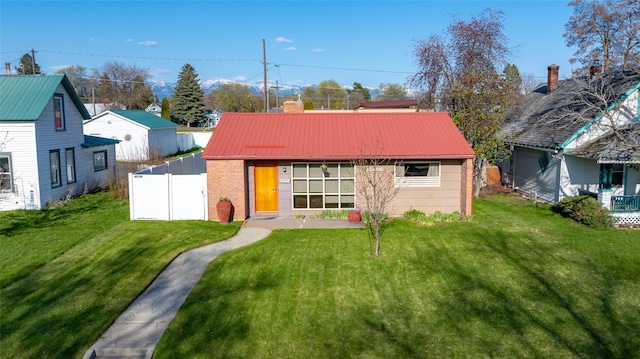 back of house with fence, a chimney, metal roof, a lawn, and brick siding