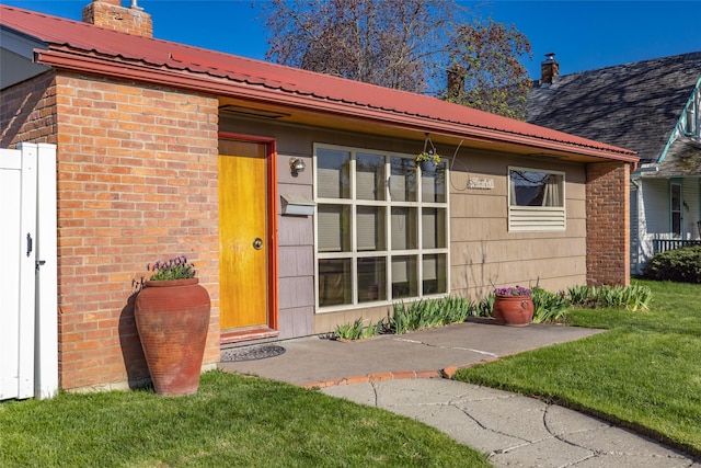 doorway to property featuring a chimney, metal roof, a yard, and brick siding