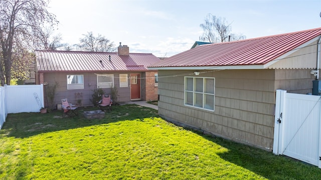 back of house featuring a chimney, a yard, a gate, fence, and metal roof