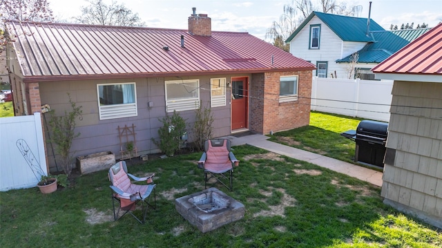 back of house with a chimney, a fenced backyard, a yard, brick siding, and a fire pit
