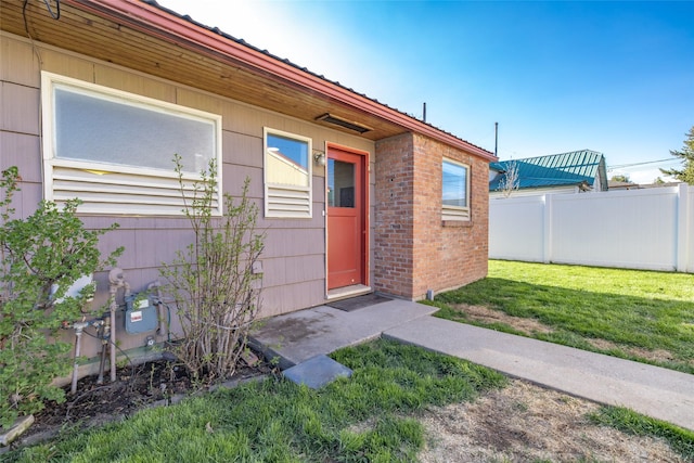 property entrance featuring brick siding, fence, and a lawn