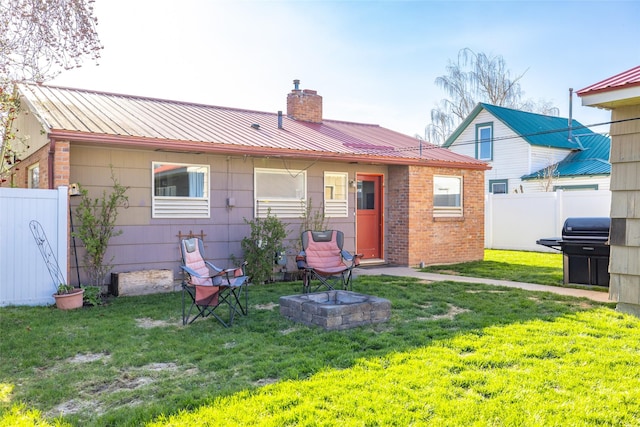 back of house featuring a chimney, an outdoor fire pit, fence, metal roof, and a lawn