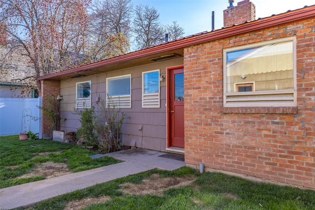 entrance to property with brick siding, fence, and a chimney