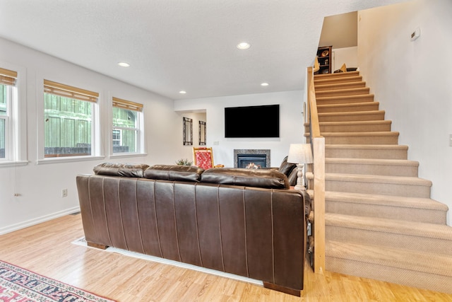 living room with a high end fireplace, recessed lighting, stairs, and light wood-type flooring