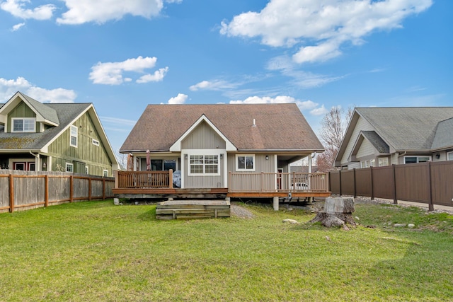 rear view of property with a lawn, a deck, a shingled roof, and a fenced backyard