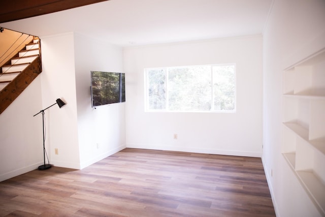 spare room with stairway, wood finished floors, ornamental molding, and baseboards
