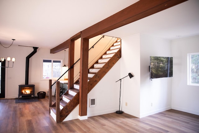 staircase with visible vents, wood finished floors, a healthy amount of sunlight, and a wood stove