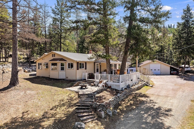 view of front of house featuring a wooden deck, an outbuilding, a detached garage, driveway, and a chimney