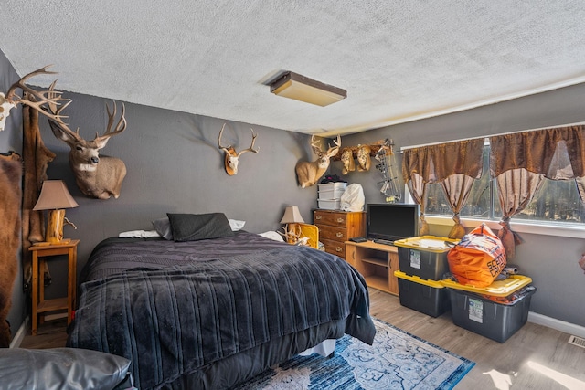 bedroom featuring a textured ceiling, wood finished floors, visible vents, and baseboards
