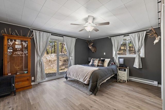 bedroom with multiple windows, access to outside, wood finished floors, and a baseboard radiator