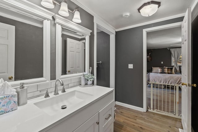bathroom with wood finished floors, backsplash, vanity, baseboards, and crown molding