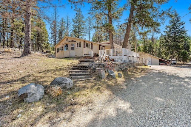 view of front facade with gravel driveway, a wooden deck, and an outbuilding