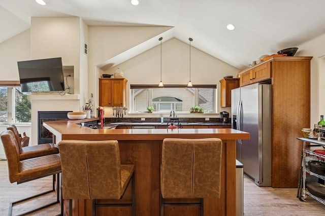 kitchen with light wood-style floors, stainless steel fridge, brown cabinetry, a glass covered fireplace, and a breakfast bar area