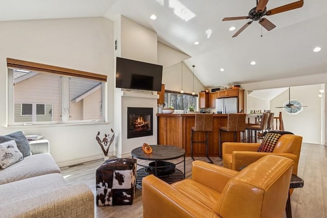 living room with light wood-style floors, a glass covered fireplace, recessed lighting, a ceiling fan, and high vaulted ceiling