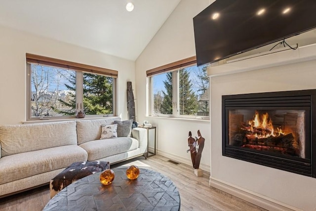 interior space with light wood-style floors, visible vents, baseboards, a glass covered fireplace, and high vaulted ceiling