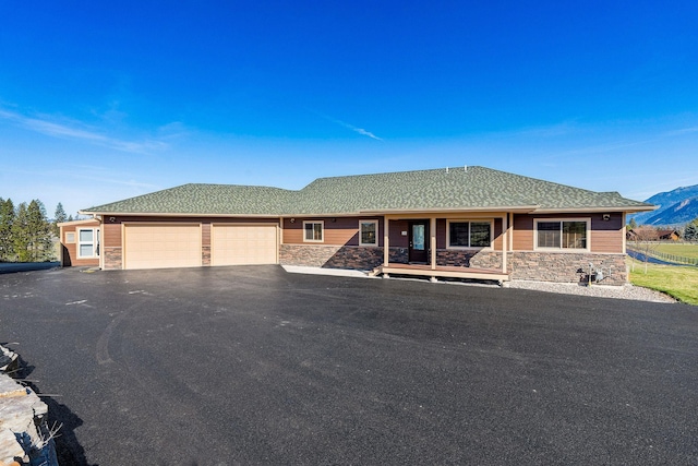 ranch-style home with covered porch, aphalt driveway, a garage, stone siding, and a mountain view