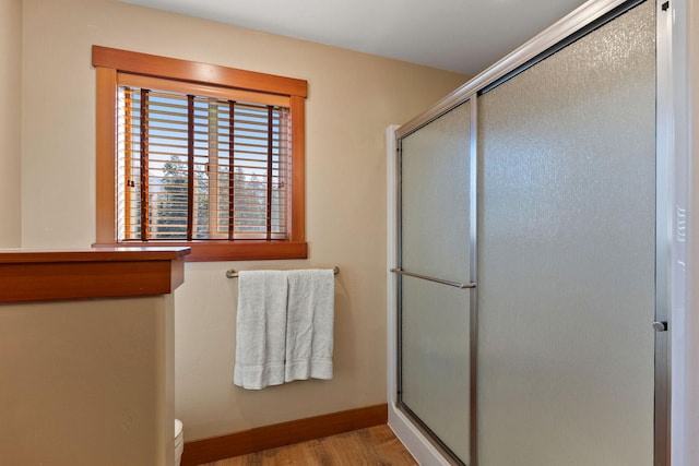 bathroom featuring toilet, a shower with shower door, wood finished floors, and baseboards
