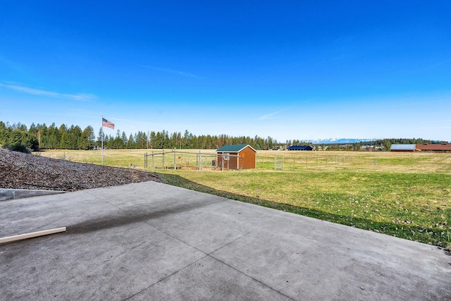 view of yard featuring fence, an outdoor structure, a rural view, and a storage unit