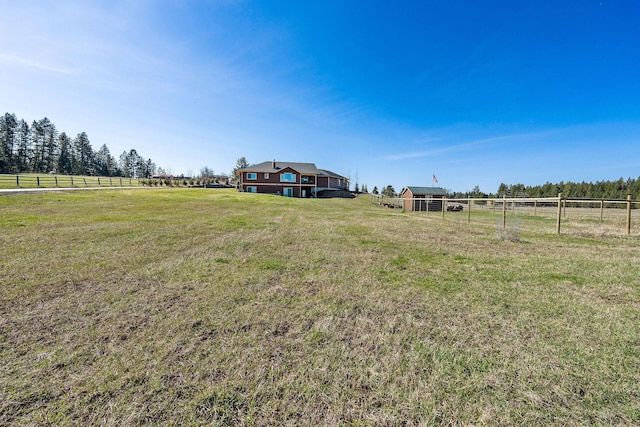 view of yard with fence, an outdoor structure, and a rural view