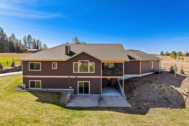 back of house with roof with shingles, a chimney, a patio area, and a yard