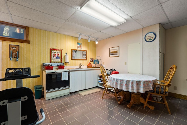 kitchen featuring dark tile patterned flooring, a drop ceiling, range with electric stovetop, rail lighting, and a sink