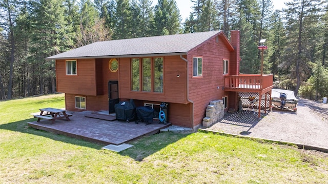 rear view of property with a deck, a chimney, a shingled roof, a patio area, and a lawn