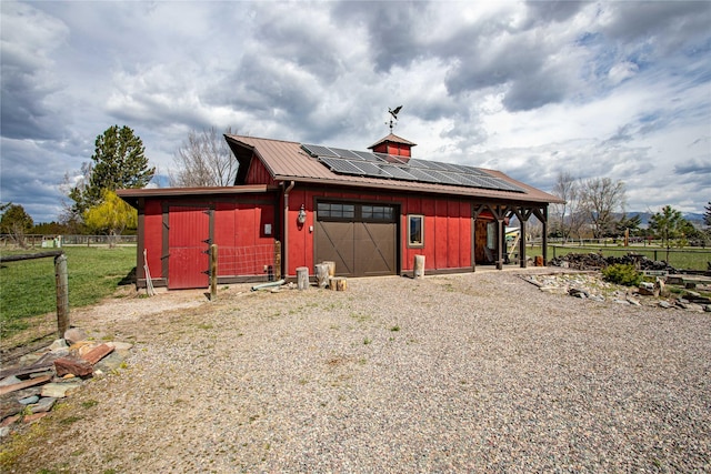 view of outbuilding featuring fence, an outbuilding, solar panels, driveway, and an attached garage