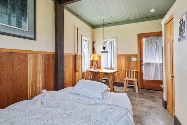 bedroom featuring wooden walls, concrete floors, and a wainscoted wall