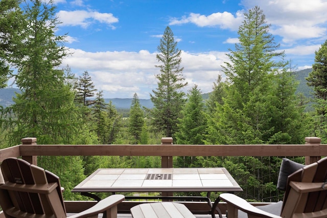 wooden deck featuring a mountain view, outdoor dining space, and a forest view
