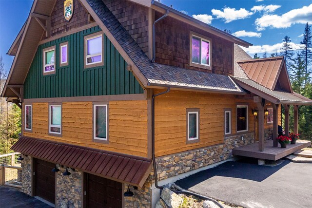 view of property exterior featuring board and batten siding, a shingled roof, an attached garage, and stone siding